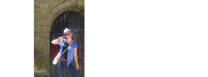 Karen Berry in a blue t-shirt and hat, standing in a stone archway