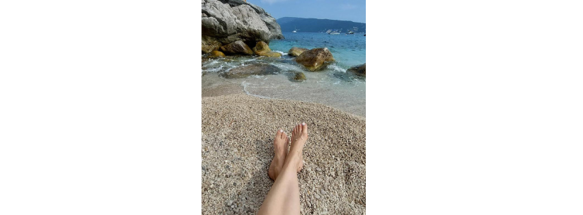 Bare feet resting on wet sand at the edge of the water