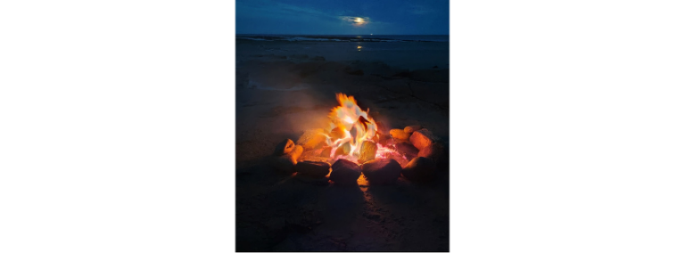 A campfire burning on a beach at night, stones glowing around it