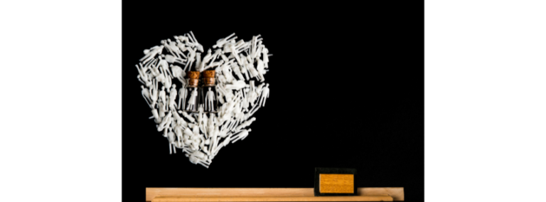 Two small amber bottles surrounded by white petals arranged in a heart on black