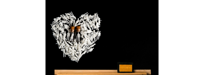 Two small amber bottles surrounded by white petals arranged in a heart on black