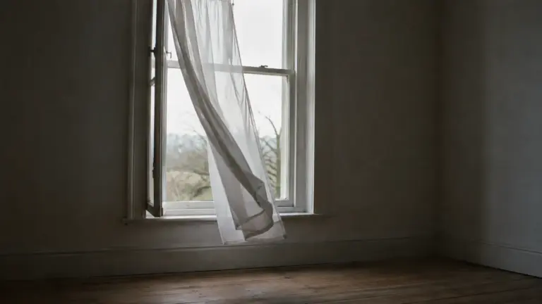 An open window with a net curtain lifting in the breeze