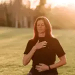 Dorothy Nelson kneeling in a field at sunset, one hand on her chest and one on her belly