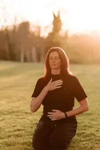 Dorothy Nelson kneeling in a field at sunset, one hand on her chest and one on her belly