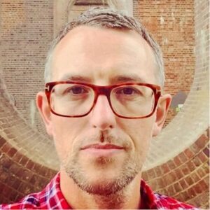 Ian King in red glasses, photographed beneath a brick archway