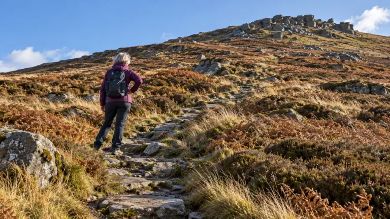 A woman pausing with a hand on her hip, part way up a moorland path