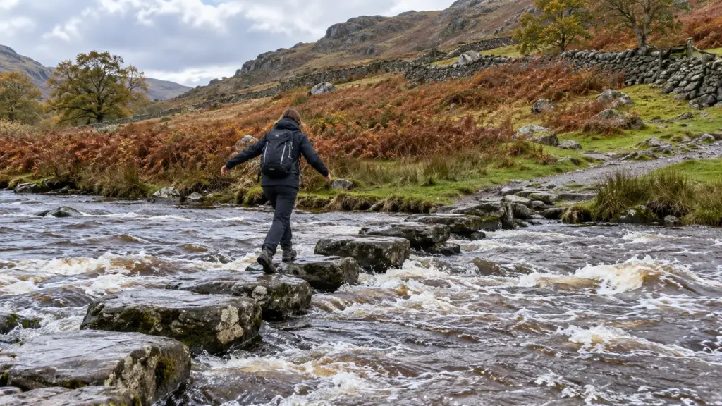 A person mid-stride across wet stepping stones over a fast brown upland river