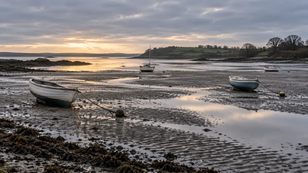 Small boats resting on wet sand at low tide in a grey early morning estuary