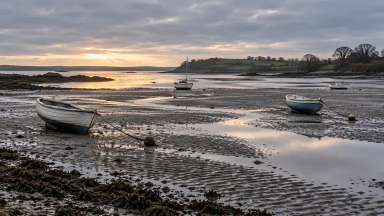 Small boats resting on wet sand at low tide in a grey early morning estuary
